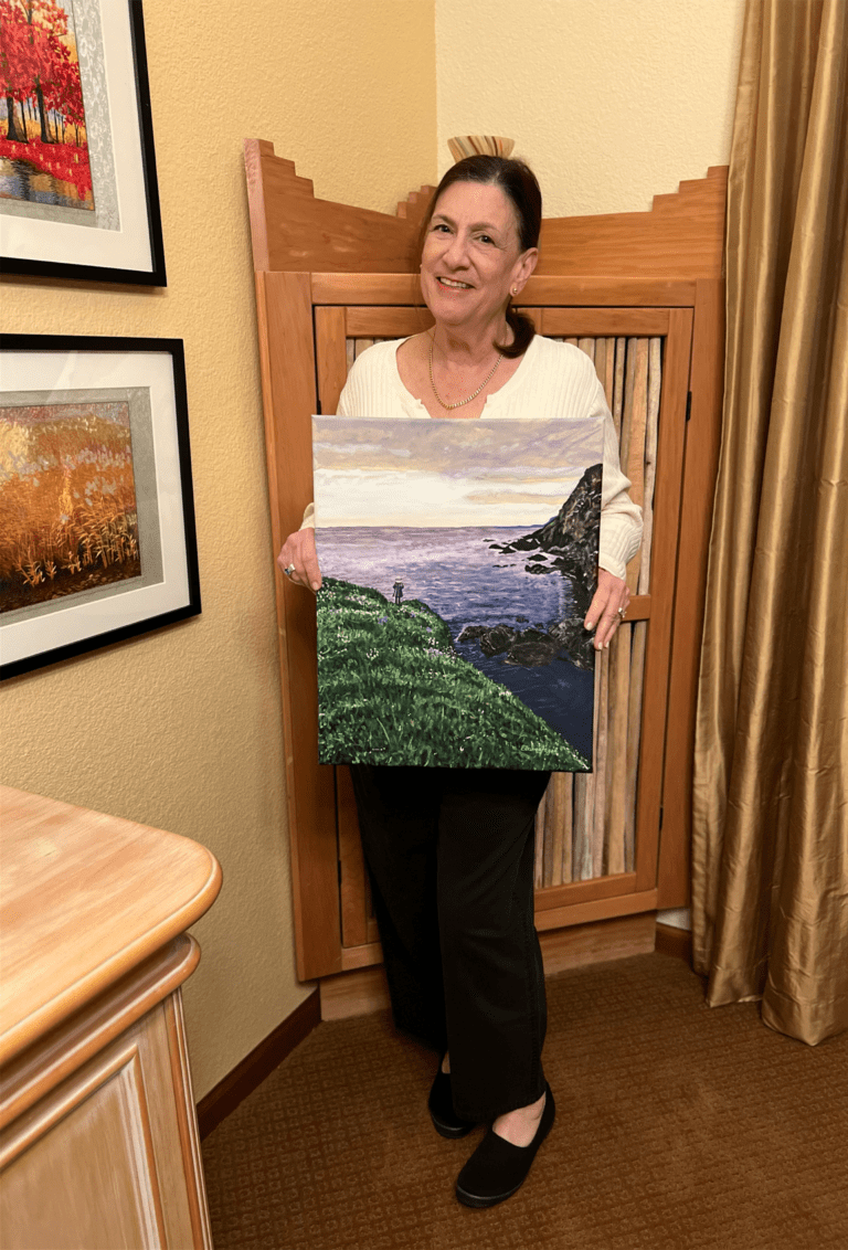 Image of artist, Elaine Fogel holding her original painting of Newfoundland entitled, "Atlantic Lookout"